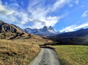 Chemin de gravier au milieu des prairies d'automne, filant droit vers les Aiguilles d'Arves saupoudrées de neige sous un ciel nuageux