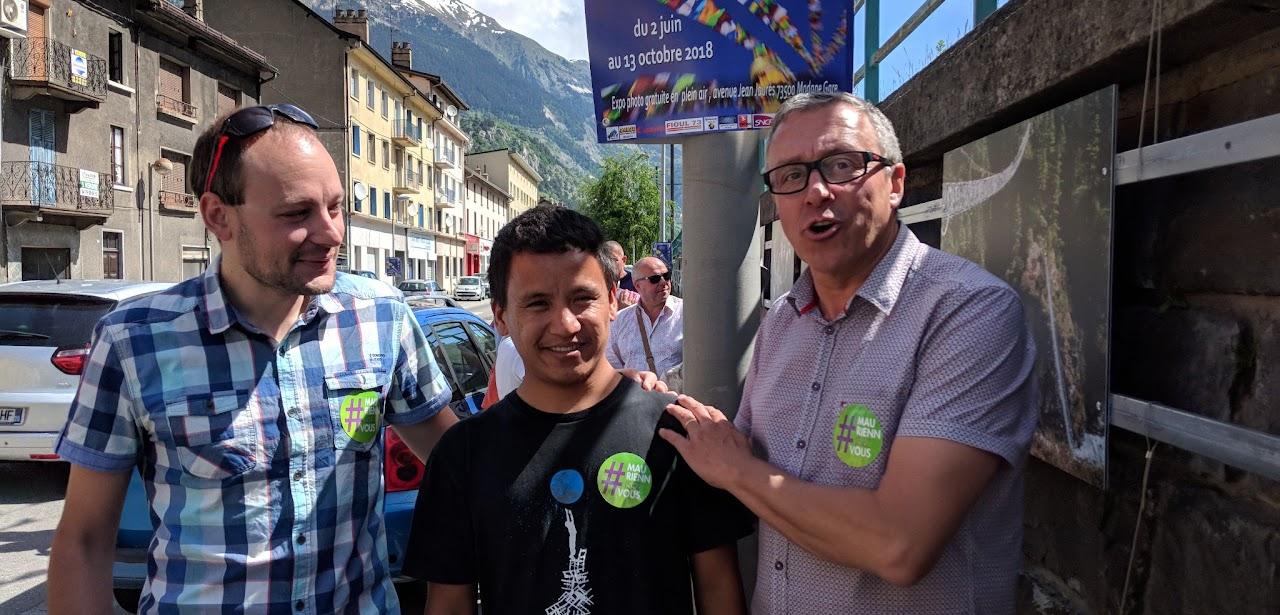 2018, trois hommes portant un autocollant #MauriennisezVous devant une banderole d'exposition photo (2 juin au 13 octobre 2018).