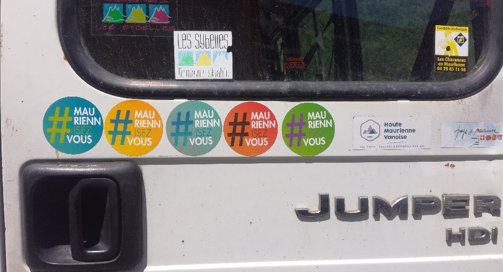 2018, portière de camionnette ornée de cinq autocollants #MauriennisezVous à côté du logo du domaine skiable Les Sybelles.