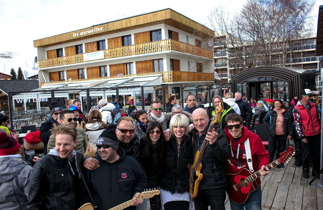 2018, groupe de musiciens et de bénévoles posant guitares à la main, terrasse du restaurant Les Marmottes, lors du concert au Chamois.