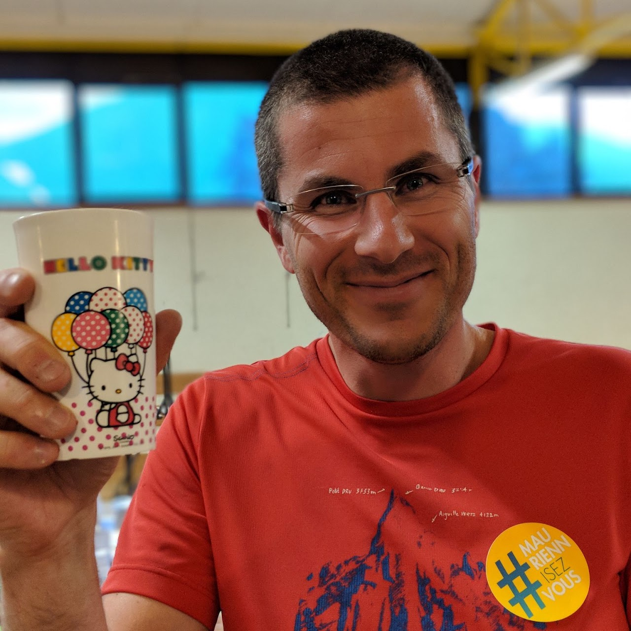 2018, un bénévole tient une tasse Hello Kitty, autocollant #MauriennisezVous sur son t-shirt, pendant la session de distribution.