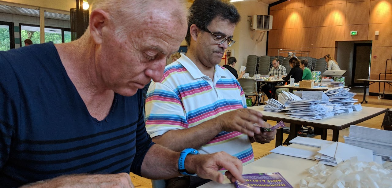 2018, deux bénévoles trient des enveloppes et un dépliant « Mauriennisez votre boîte à lettres » lors de la campagne de distribution.