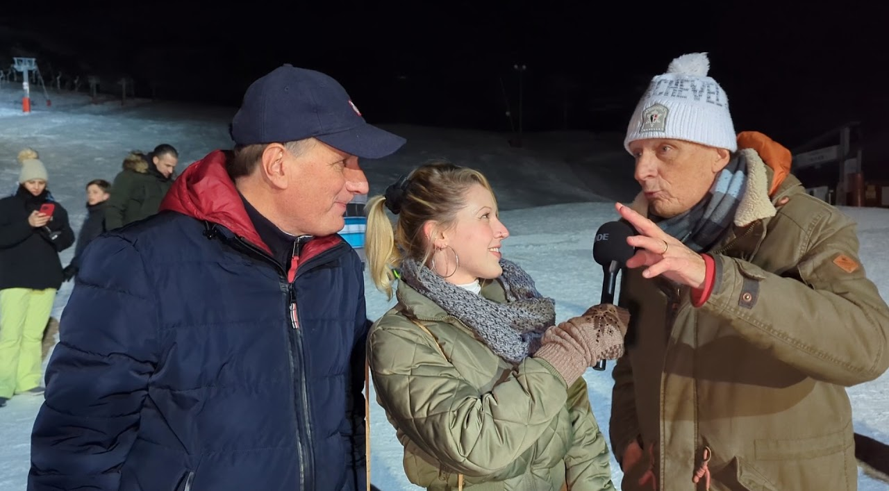 2022, Eva interviewe deux hommes de nuit à La Toussuire, station de ski illuminée en fond, micro RDE à la main.