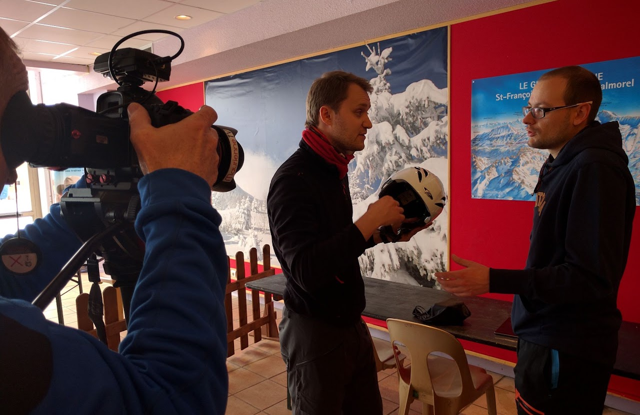 2016, Florian interviewe un homme tenant un casque de ski, à Saint-François-Longchamp, devant une affiche du domaine skiable.
