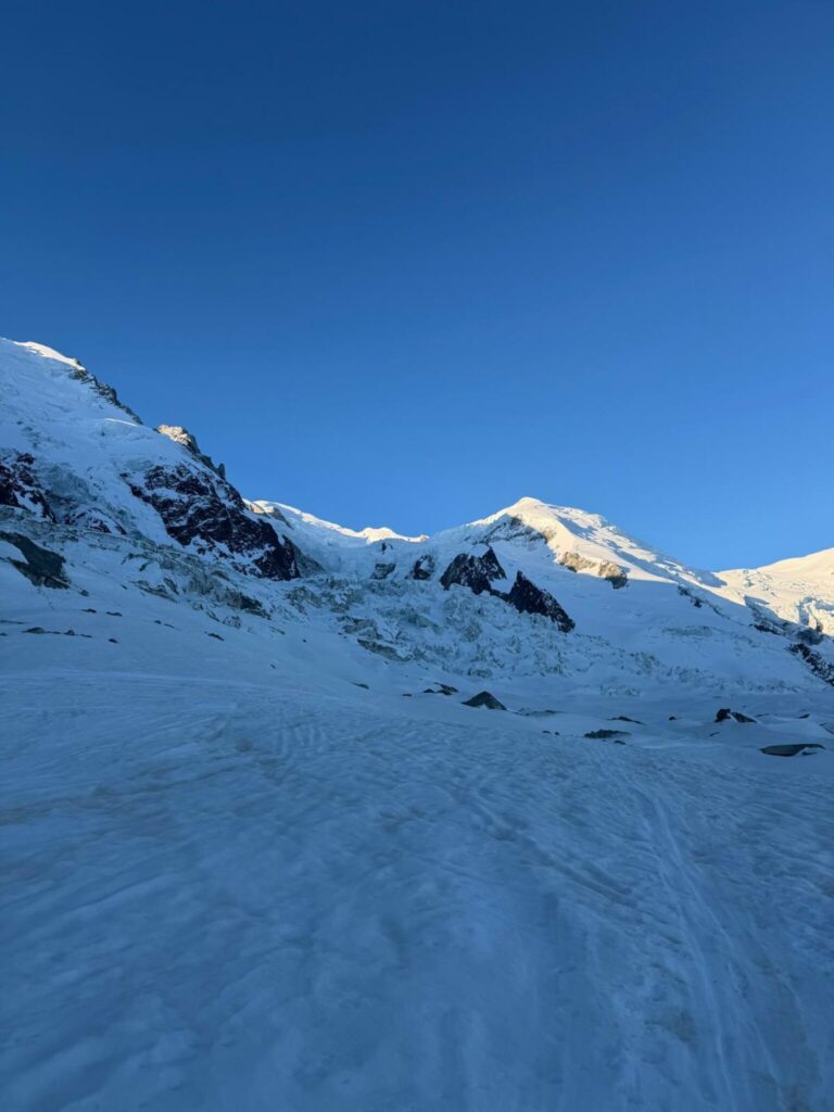 Un glacier enneigé au petit matin, avec des sommets éclairés par le soleil sous un ciel bleu