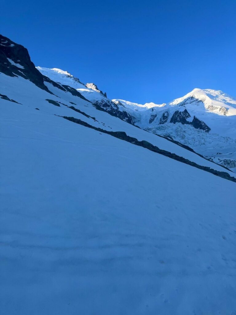 Haute montagne enneigée sous un ciel bleu, avec de grandes pentes à l'ombre et des sommets glacés au fond