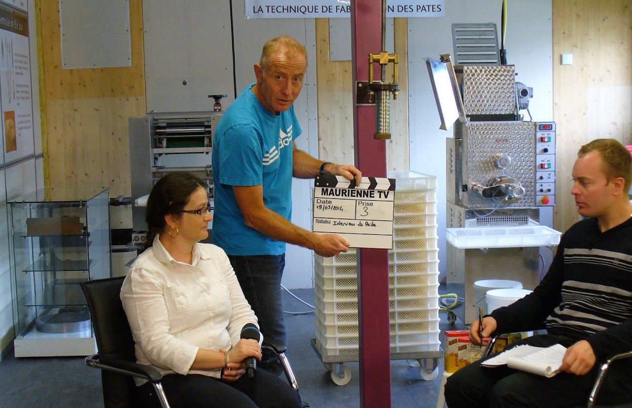19 mars 2014, tournage avec Cédric : clap « Maurienne TV, interview la pasta » devant une machine à fabriquer des pâtes, une intervieweuse assise à gauche.