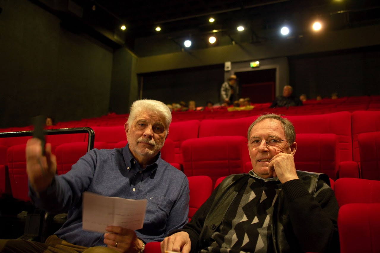 2011, interview de Jean-Claude dans la salle d'un cinéma, sièges rouges, avec un autre membre de l'équipe tenant des notes et une télécommande.