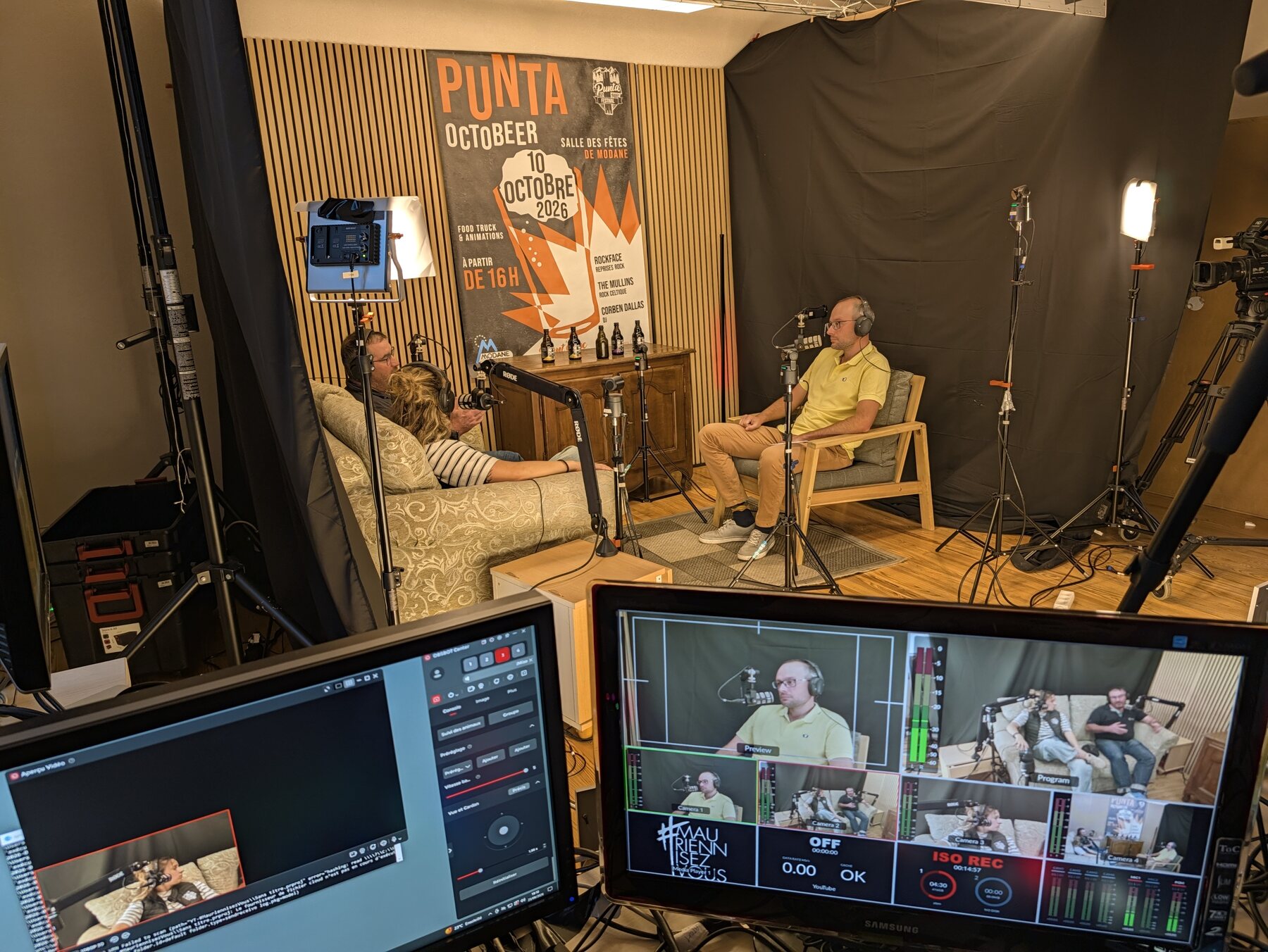 Studio MAUZ pendant le tournage du Quart d'Heure Mauriennais : l'interview des deux invités de Punt'assoc, assis sur le canapé, devant l'affiche du festival et des bouteilles de bière, avec les écrans de régie au premier plan