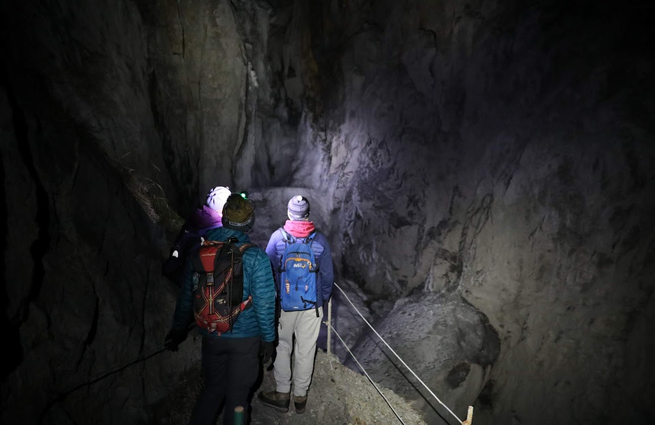 2021, sortie de cohésion nocturne : trois membres de l'équipe, frontales allumées, traversent une galerie de mine sur un sentier sécurisé par une main courante.