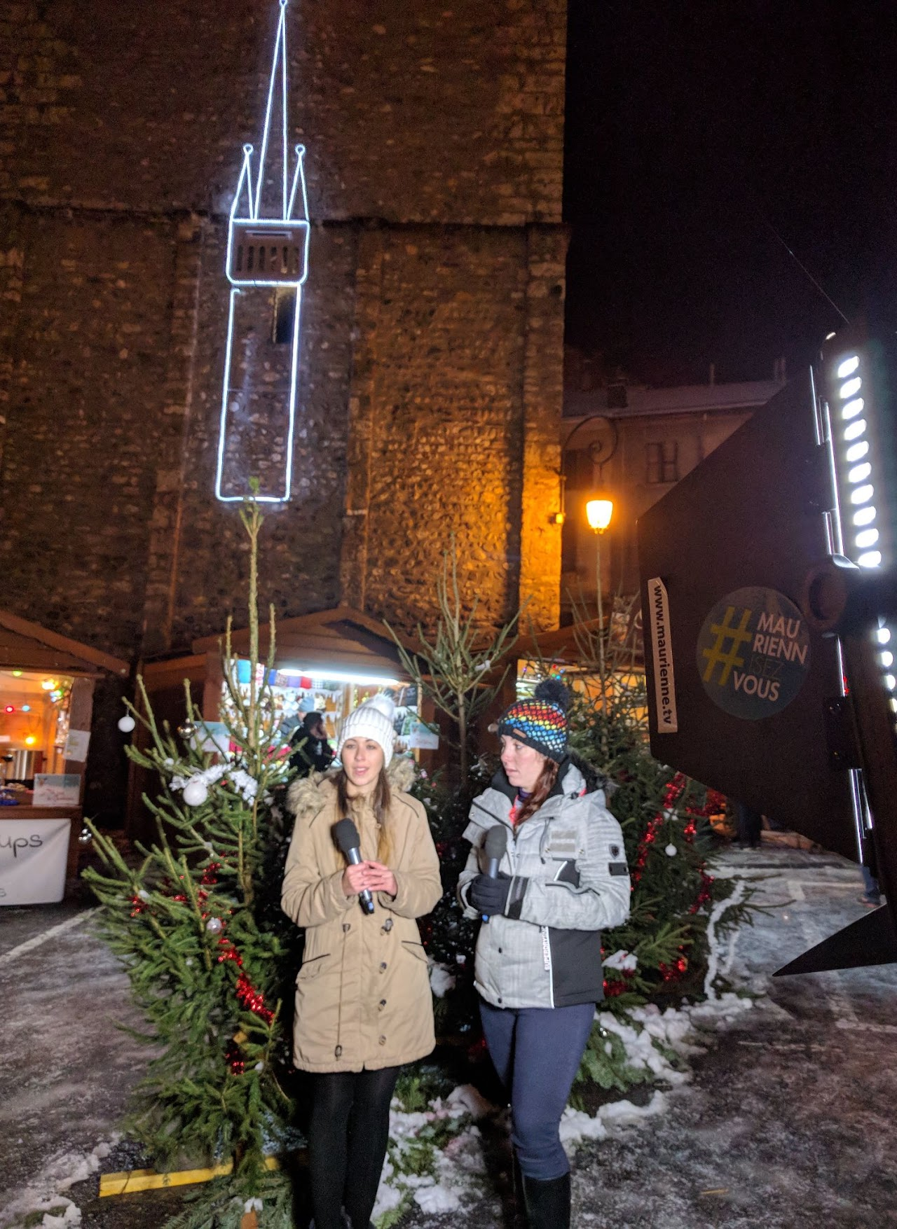 2017, marché de Noël avec Aurore : deux présentatrices au micro devant les sapins illuminés, logo #MauriennisezVous visible sur le studio mobile.
