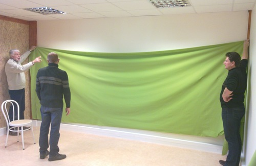 2011, trois bénévoles installent le grand tissu vert sur le mur du nouveau studio, à la pépinière Créapole.
