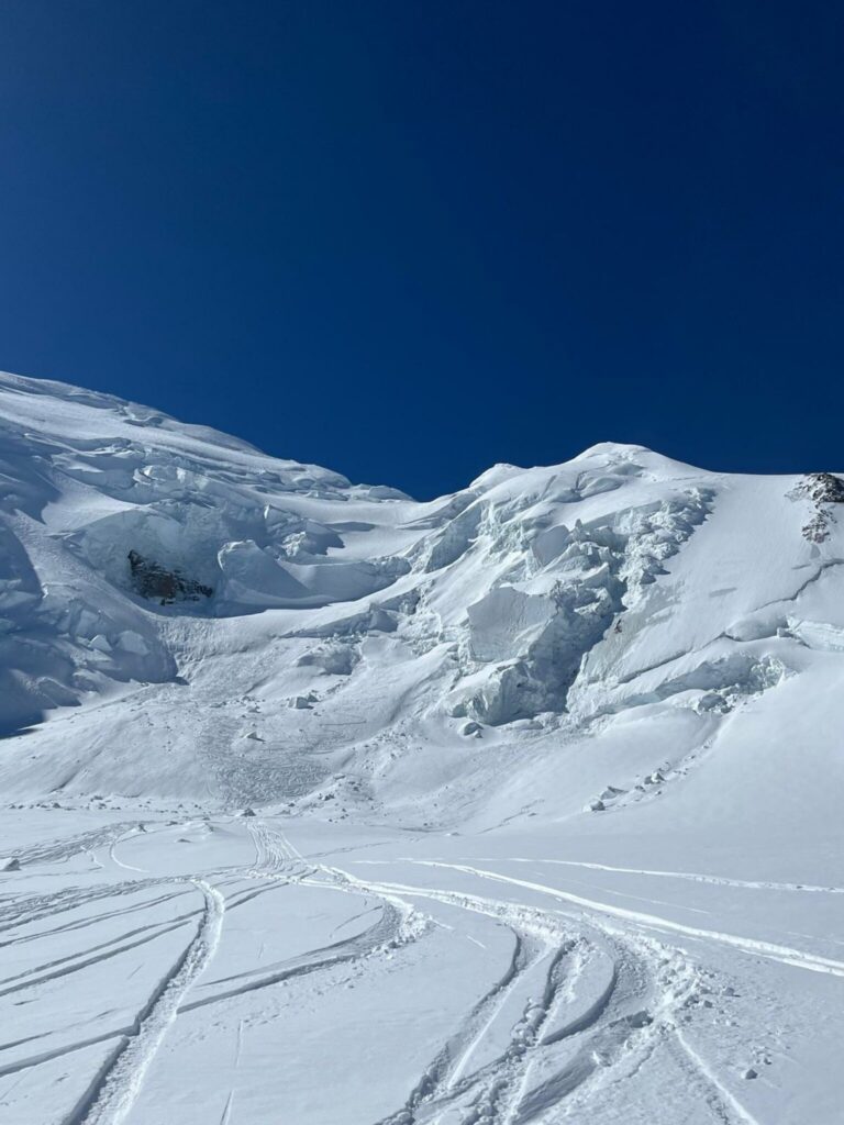 Une pente de neige marquée de traces de ski, avec des séracs et une crête enneigée en arrière-plan