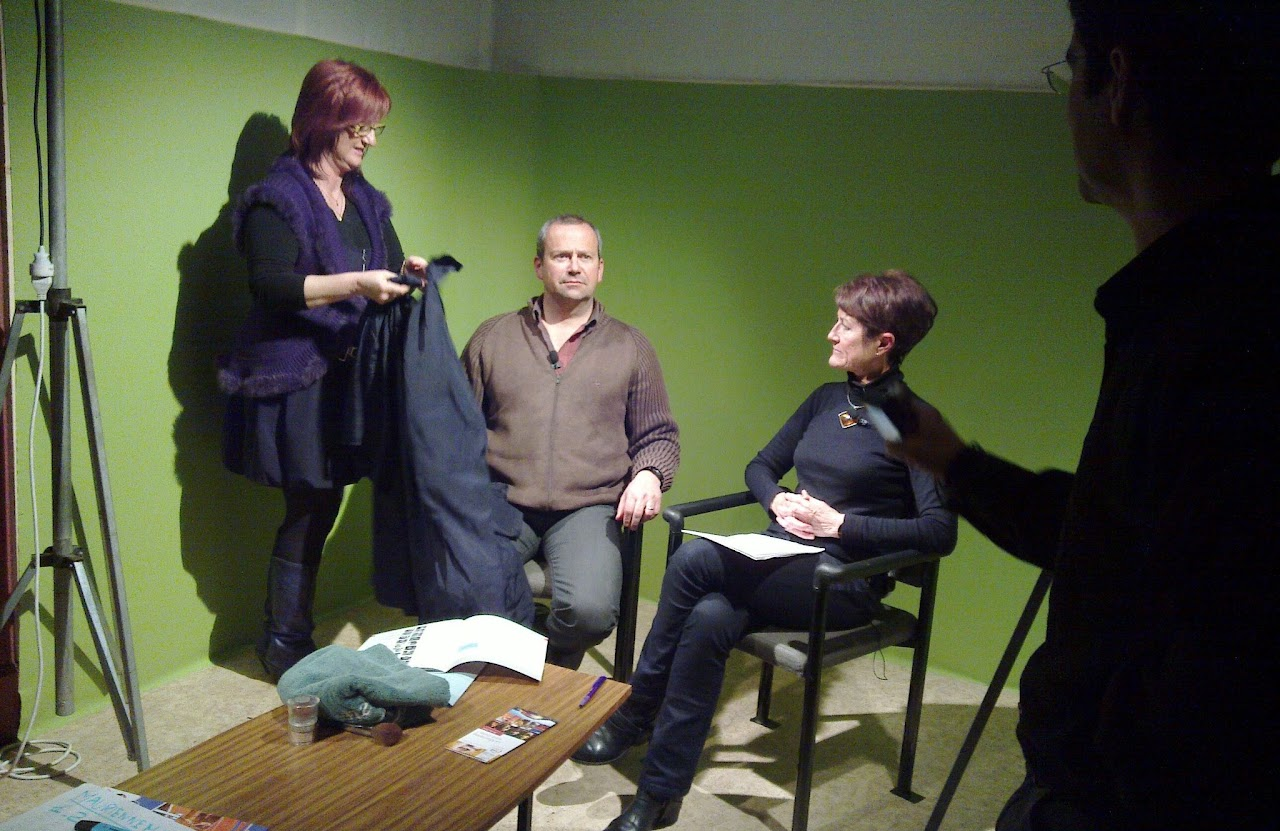 Premier studio à fond vert de Maurienne TV en 2010 : deux personnes assises pour une interview, une bénévole ajuste un vêtement avant le tournage, un cameraman au premier plan.