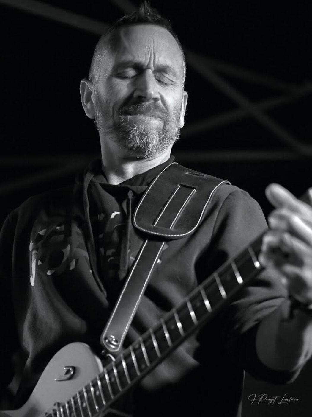 Photo en noir et blanc d'un guitariste du groupe Rockface en concert, les yeux fermés, la main sur le manche de sa guitare