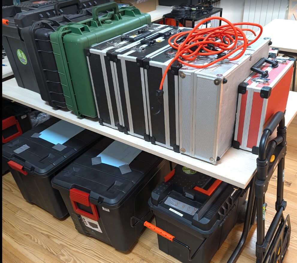 Malles de transport noires et vertes, valises métalliques et rouleau de câble orange préparés sur une étagère du studio de l’association