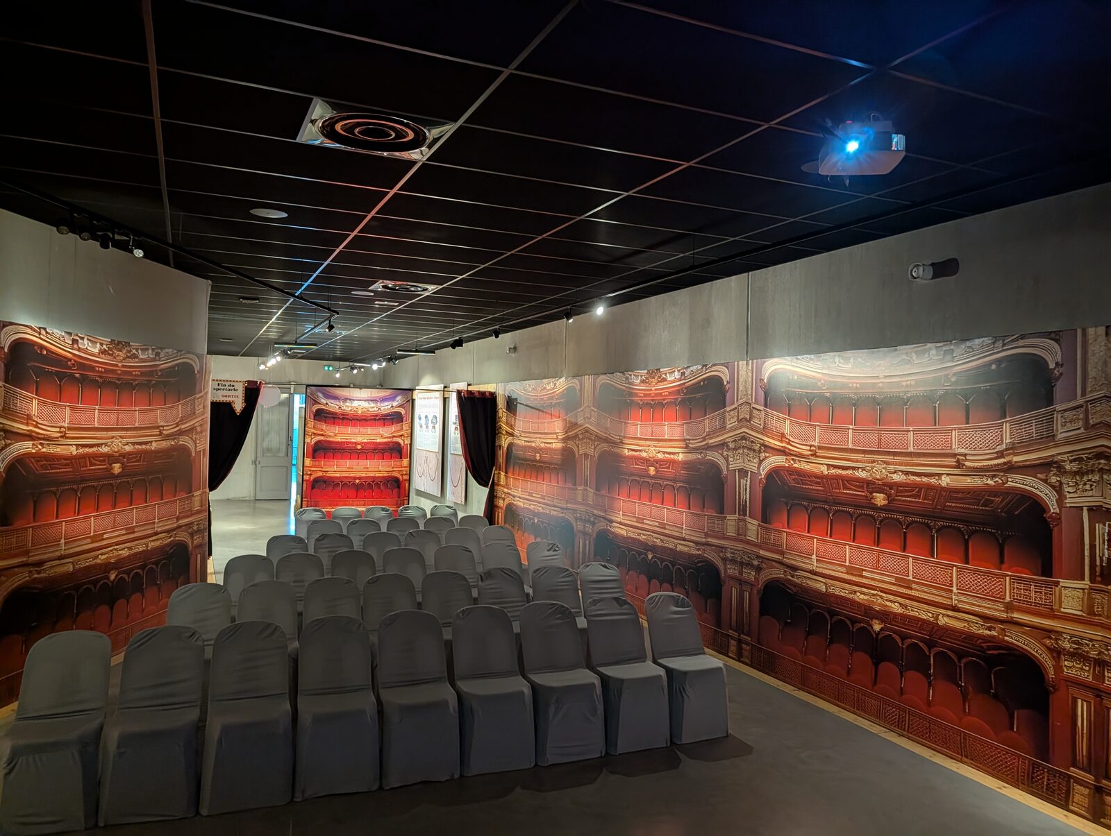 Salle de projection vide du Musée Opinel lors du repérage : rangées de chaises à housses grises et décor mural en trompe-l’œil représentant une salle de théâtre à l’italienne