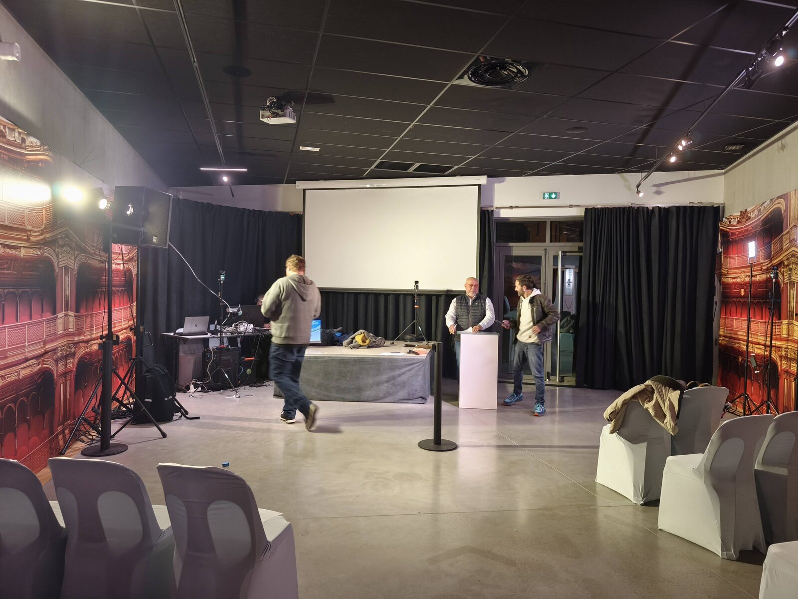 Répétition la veille du direct dans la salle du Musée Opinel : écran de projection, enceinte sur pied, table de régie installée et trois personnes en train de préparer le plateau