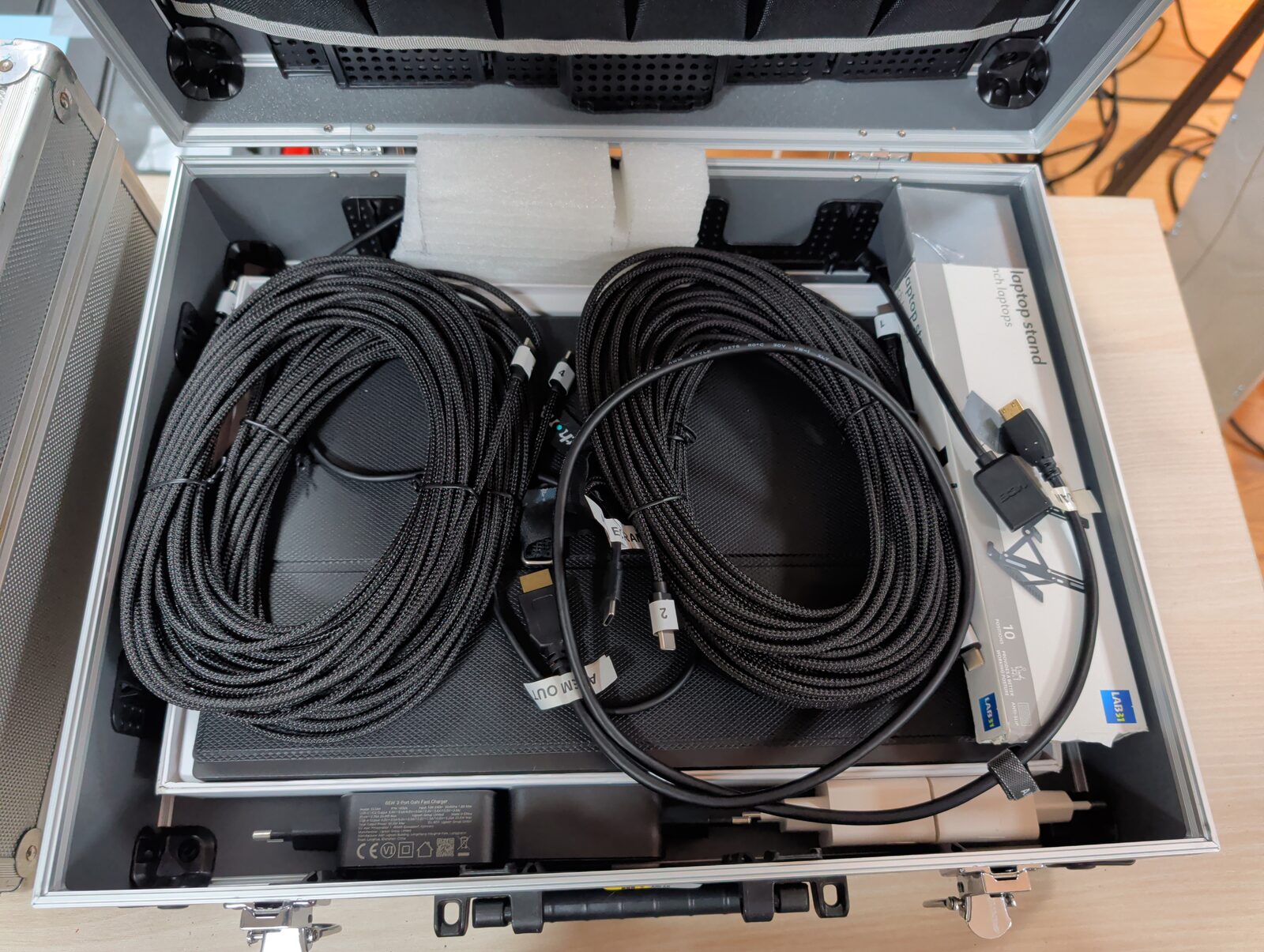 Valise de transport ouverte contenant deux longs câbles HDMI enroulés et étiquetés, un support d’ordinateur portable et un bloc d’alimentation