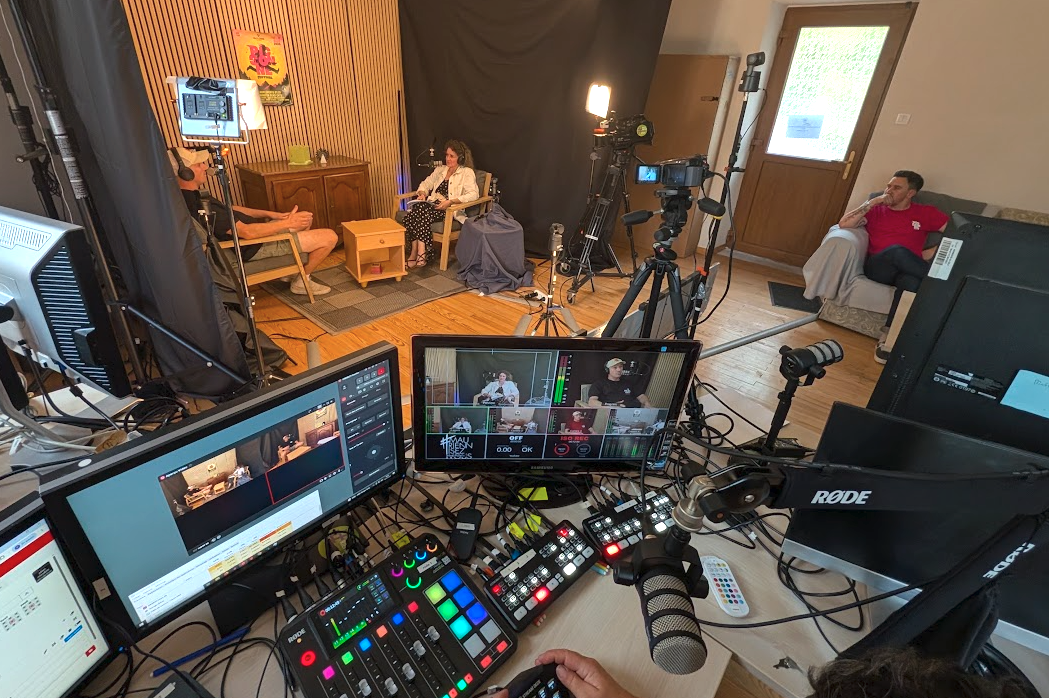 La régie et le studio de #MauriennisezVous pendant un tournage : caméras PTZ, éclairages, table de mixage vidéo Blackmagic et micros RODE au premier plan, deux invités assis face caméra à l'arrière-plan.