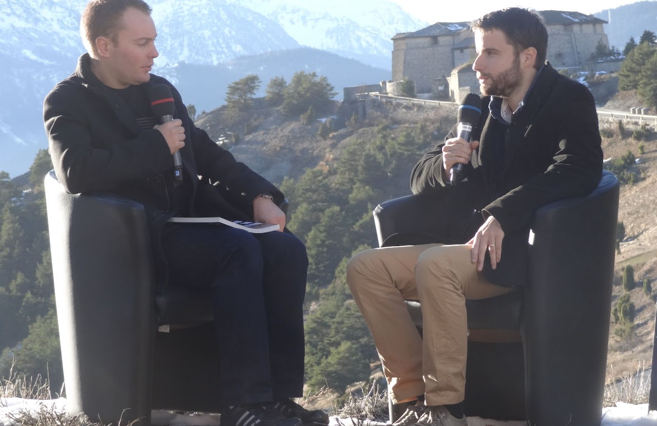 2013, tournage avec Cédric : deux hommes interviewés assis face à face devant un fort de montagne enneigé, micros Maurienne TV à la main.