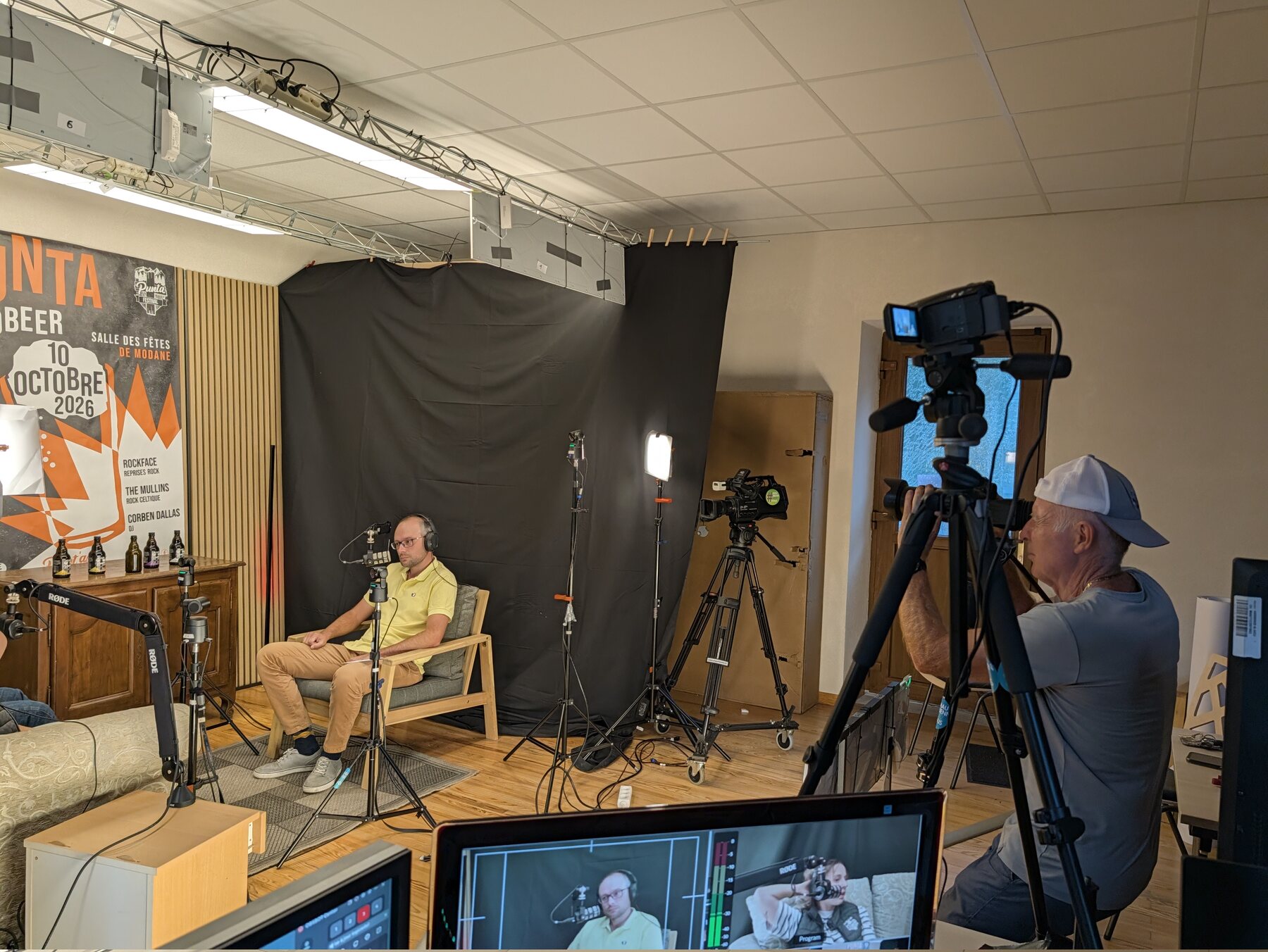 Un bénévole du studio MAUZ filme l'interview à la caméra sur pied pendant que l'intervieweur écoute ses invités, à Saint-Michel-de-Maurienne