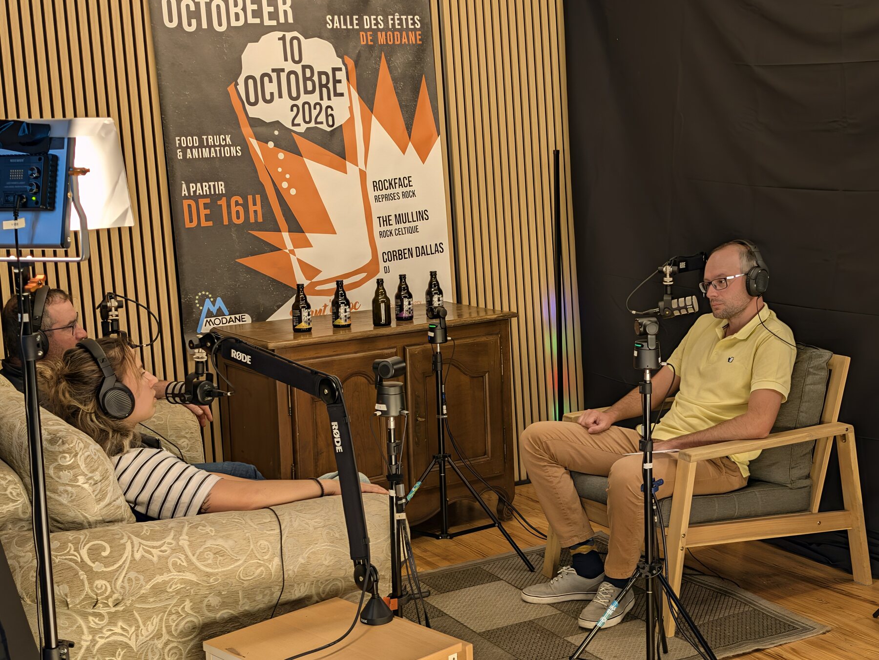 Un bénévole du studio MAUZ, en polo jaune, face aux deux invités de Punt'assoc pendant l'enregistrement du Quart d'Heure Mauriennais, avec les bouteilles de la Brasserie des Terres Blanches posées sur le buffet sous l'affiche