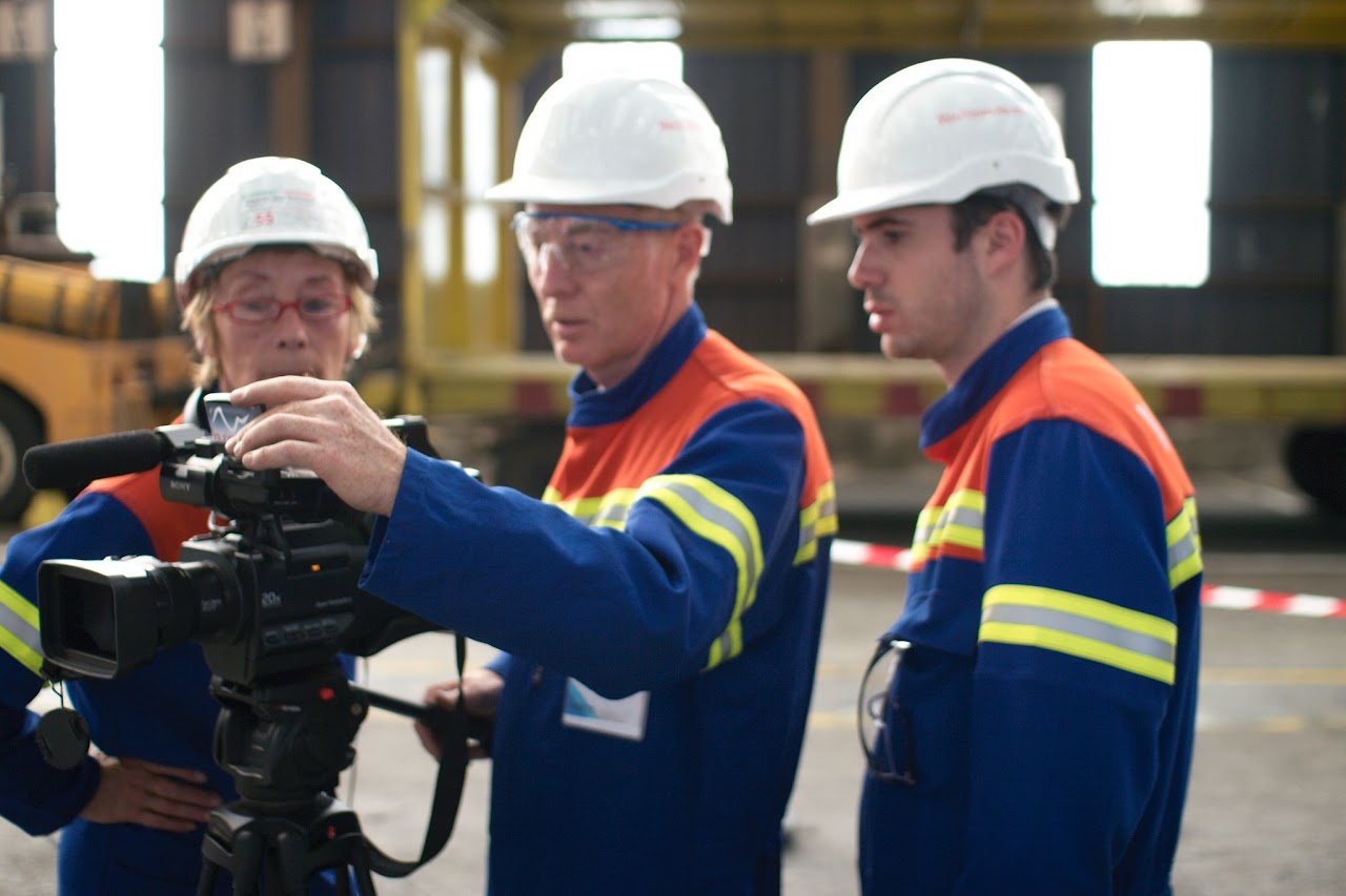 2011, trois membres de l'équipe en casque et gilet de sécurité filment avec une caméra sur pied à l'intérieur de l'usine Rio Tinto Alcan.