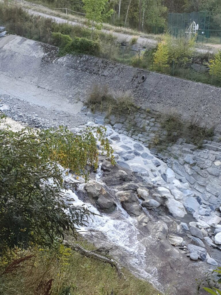 Eau du torrent du Charmaix dévalant des blocs de rocher le long d'une berge en enrochements et d'un talus bétonné