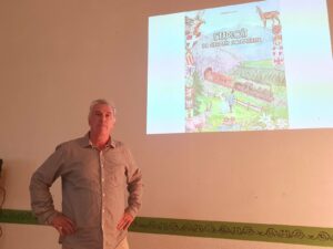 Laurent Fiorese, mains sur les hanches, devant la projection de la couverture de son livre L'exploit de Germain Sommeiller, lors de la conférence de la SHAM à Saint-Jean-de-Maurienne