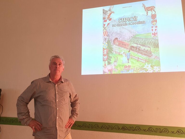 Laurent Fiorese, mains sur les hanches, devant la projection de la couverture de son livre L'exploit de Germain Sommeiller, lors de la conférence de la SHAM à Saint-Jean-de-Maurienne