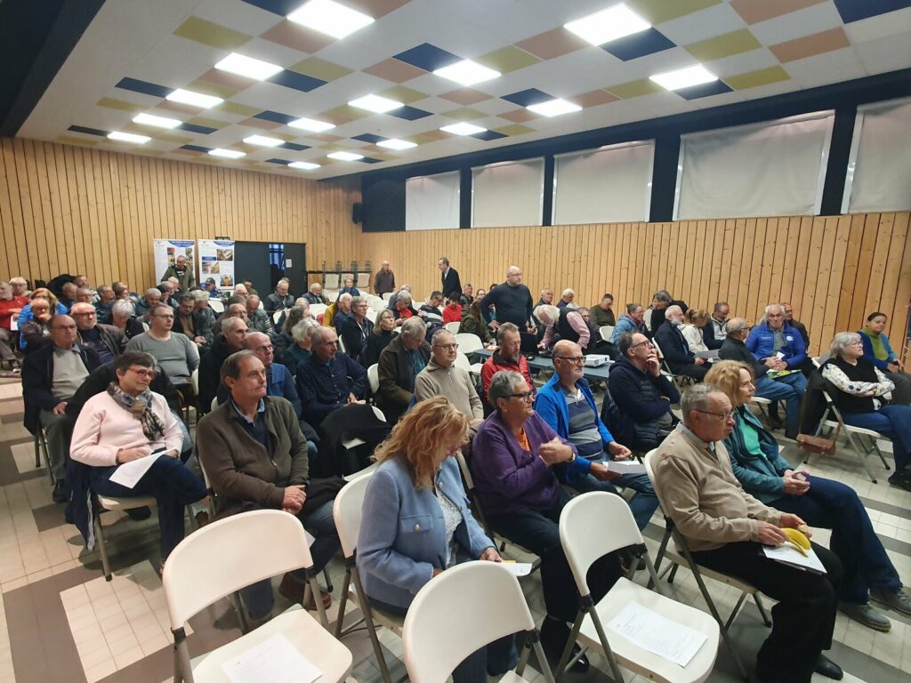 Salle du Foyer rural de Val d'Arc remplie d'apiculteurs assis sur des chaises blanches, tournés vers l'écran avant la conférence sur le pollen