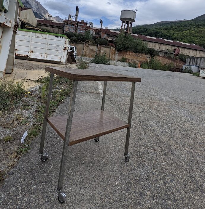 Table à roulettes sur le parking du site de l'usine Métal Temple, utilisée pour transporter les documents sauvés ; bâtiments et château d'eau au fond