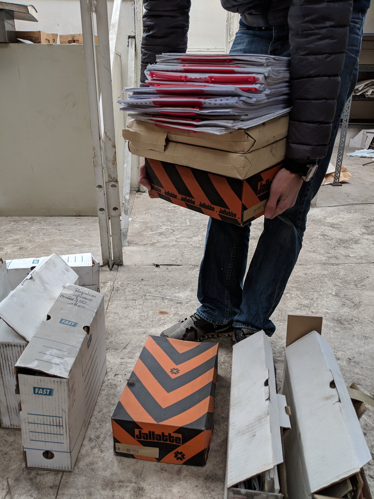 François porte une pile de cartons d'archives dans l'usine Métal Temple en novembre 2018